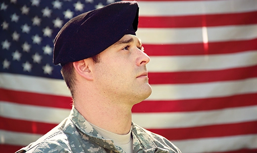 A US military member in uniform, in front of an American flag