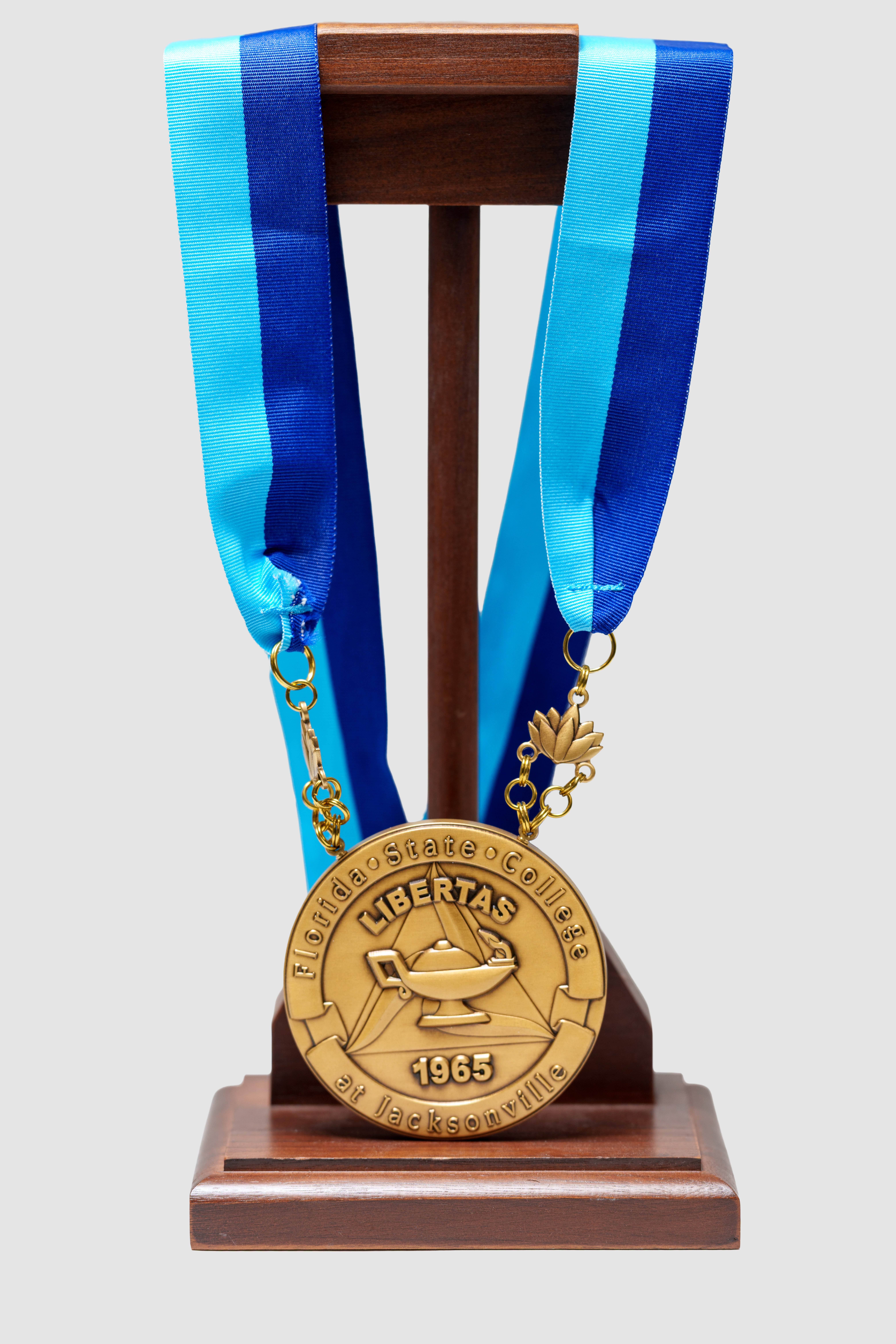 The FSCJ President's Insignia of Office is a gold-colored medallion attached to a turquoise and navy blue ribbon with two gold-colored chains