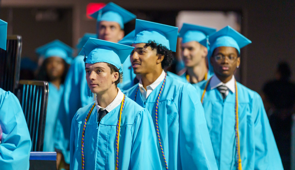 A line of FSCJ students dressed in turquoise-colored caps and gowns walking onto the floor of the Jacksonville Veterans Memorial Arena