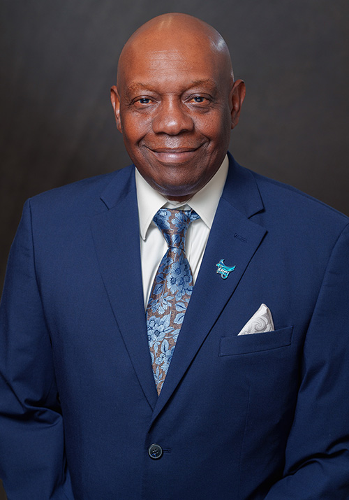 George Fredrick in navy suit jacket with floral tie on dark grey background