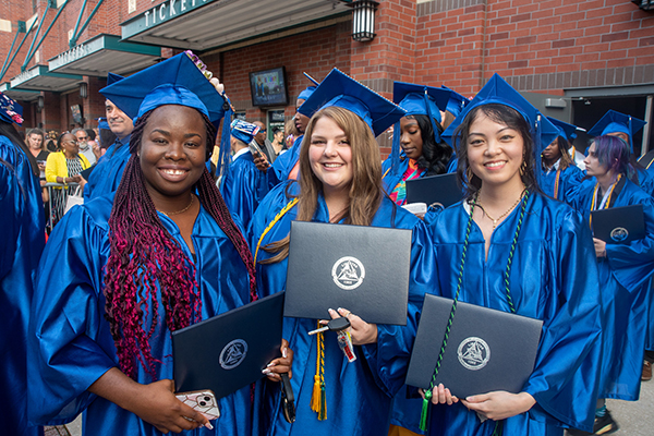 Three graduates holding diplomas