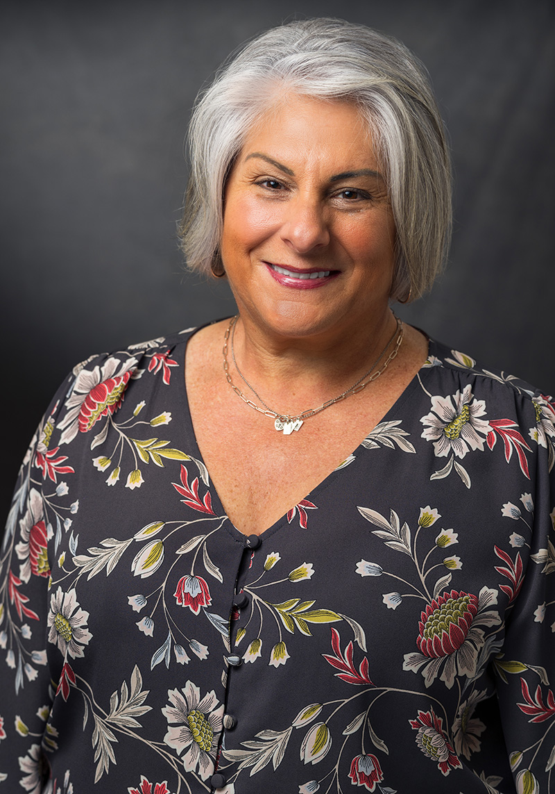 Donna Mollis Richardson in a floral top on a dark grey background