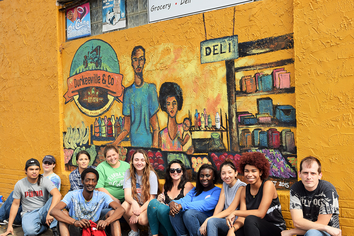 Professor Mary Jo Hinson's class and Aarion Williams in front of the mural at Durkeeville and Co. (Credit photo to The Campus Voice)