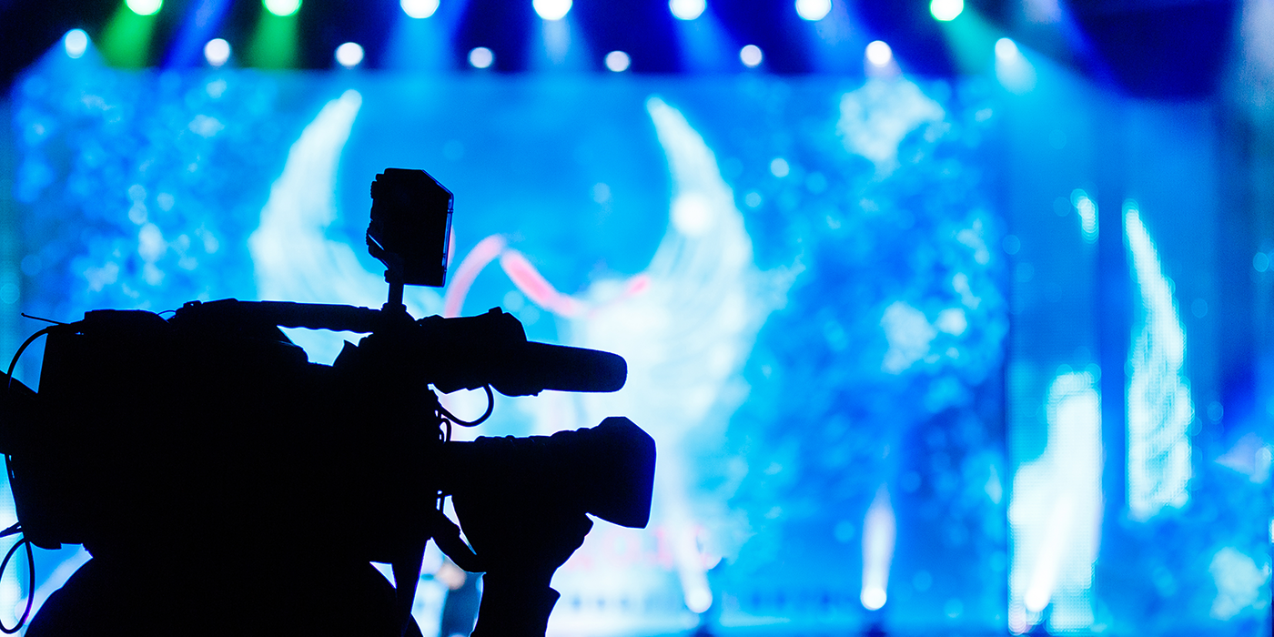 A silhouette of a person holding a large camera in front of stage lights