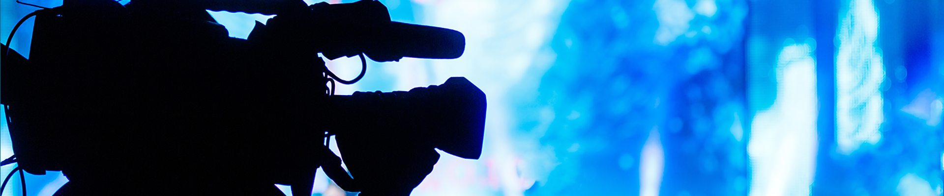 A silhouette of a person holding a large camera in front of stage lights