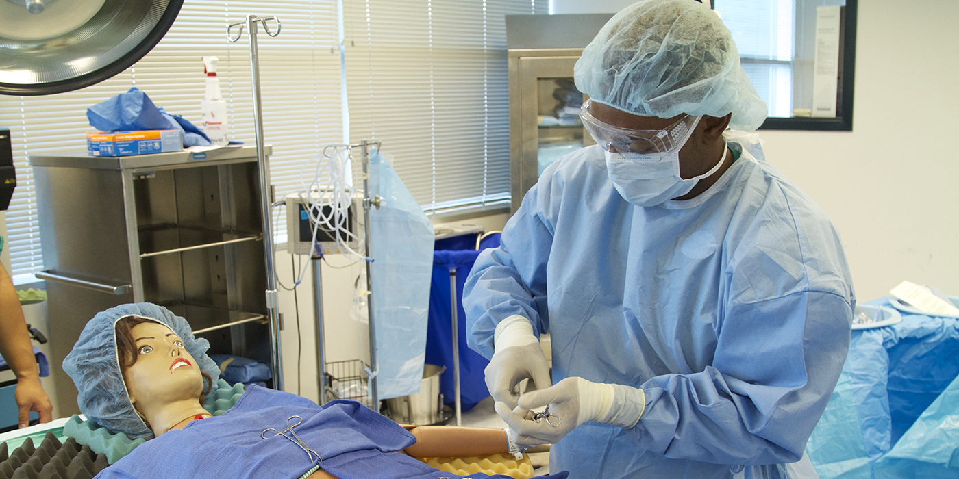 A person in full medical protective gear working on a medical dummy