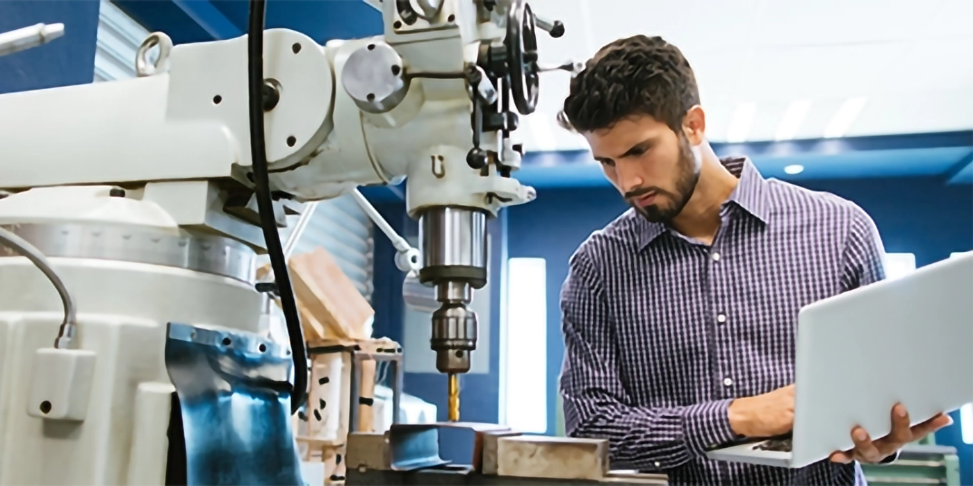 A man with a laptop using industrial equipment