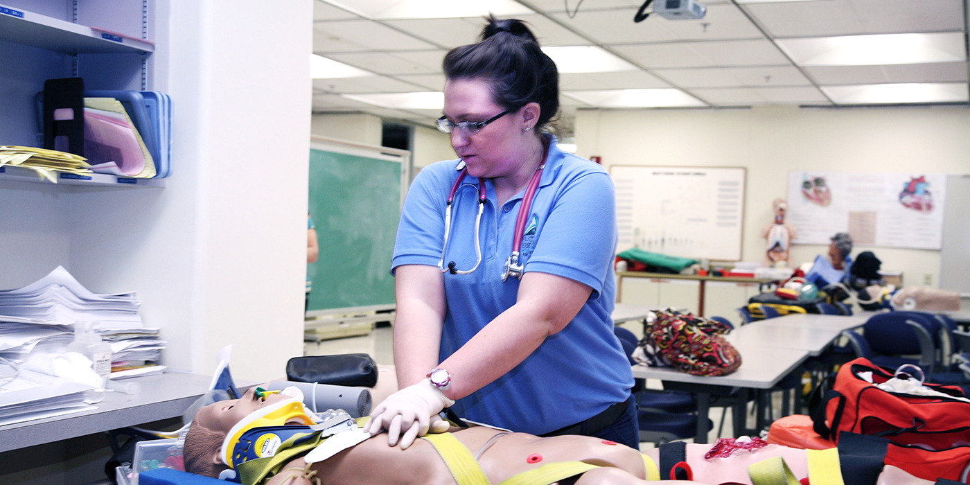 A woman in EMT gear performing CPR on a training dummy