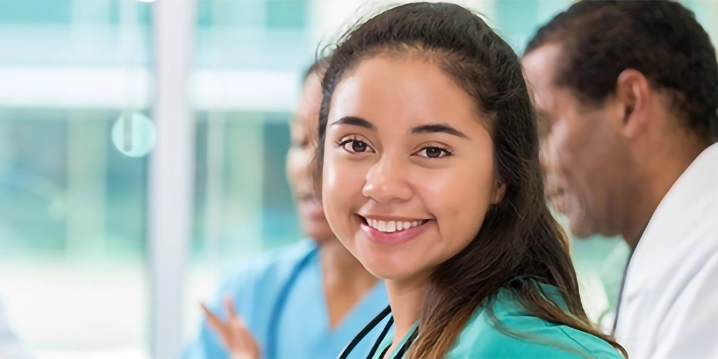 A young woman in medical scrubs with two other medical professionals behind her