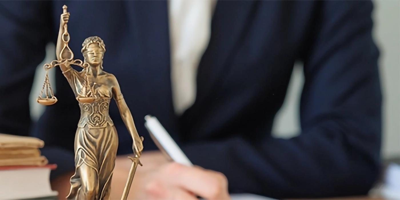 A small statue of the blind scales of justice on a desk in front of a person
