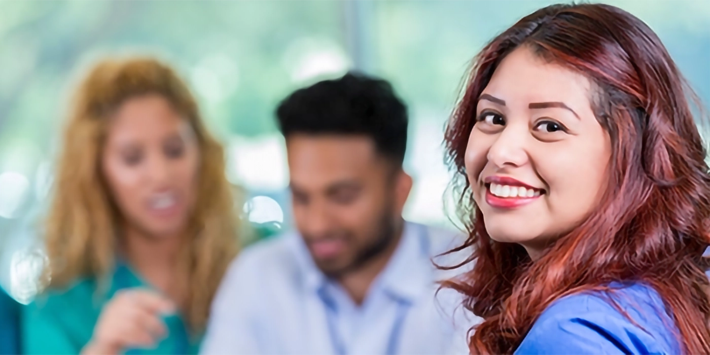 A woman smiling at the camera with two other people in the background