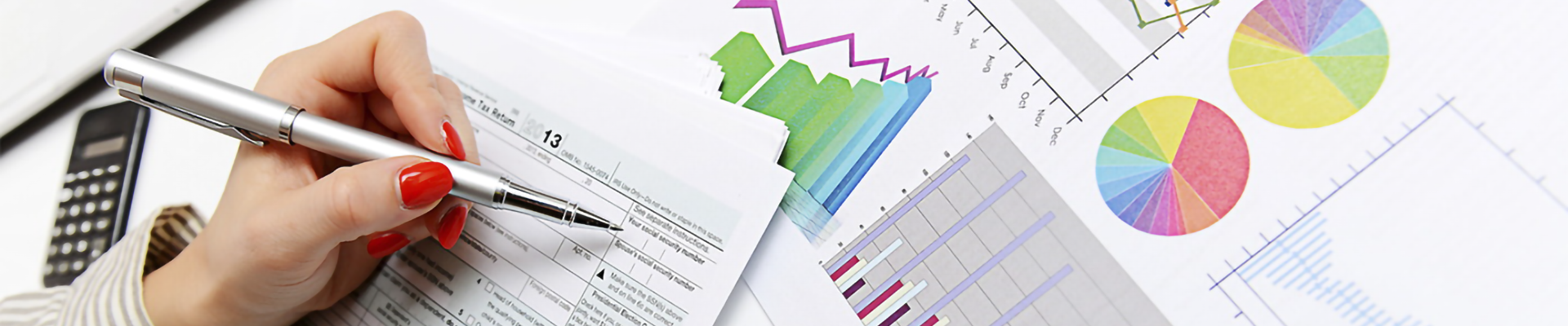 A hand holding a pen over a series of charts and forms