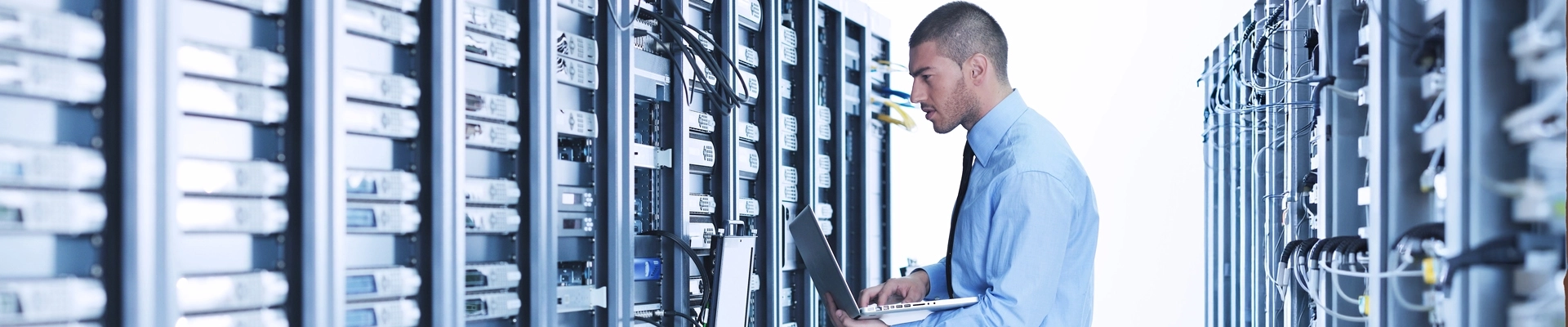 A man with a laptop in front of a network server rack