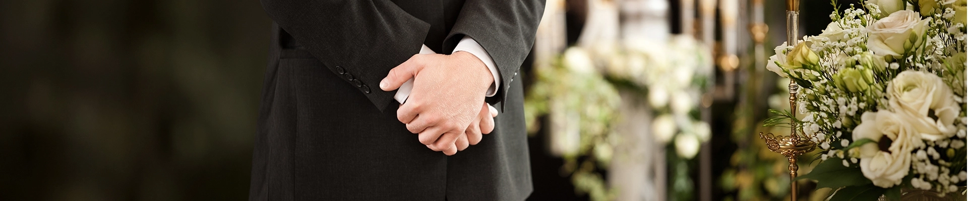 Close up of a person in a suit with crossed hands in front of a flower arrangement
