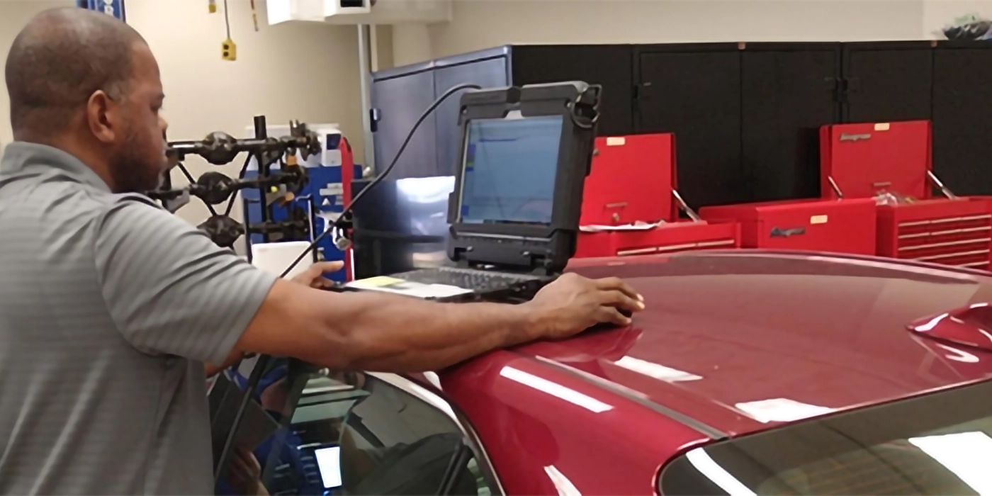 A man using a diagnostic computer on the top of a car