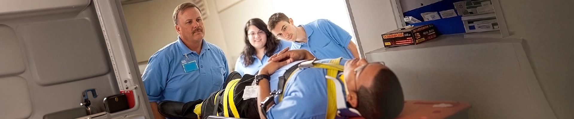 An EMT student strapped to a headboard being attended to by other EMT students
