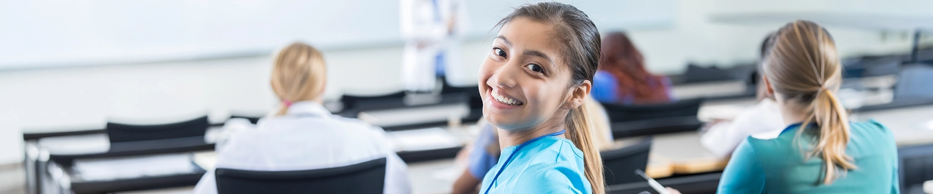 A young woman in medical scrubs with two other medical professionals behind her