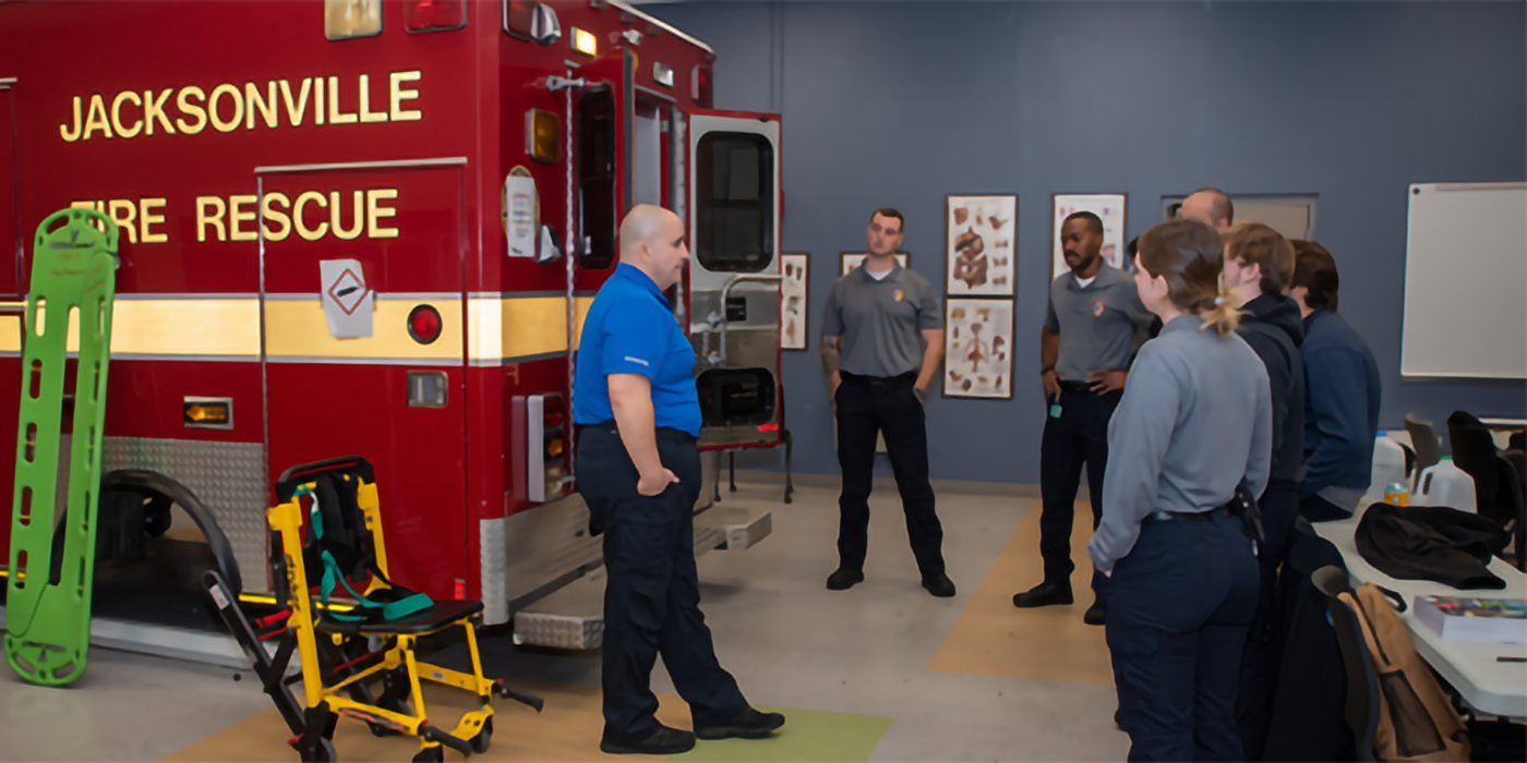 Paramedic students standing around an ambulance training mockup